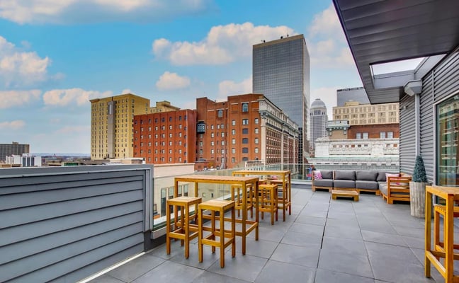 Rooftop terrace with wooden bar seating and gray sofa overlooking downtown city skyline with brick and glass buildings